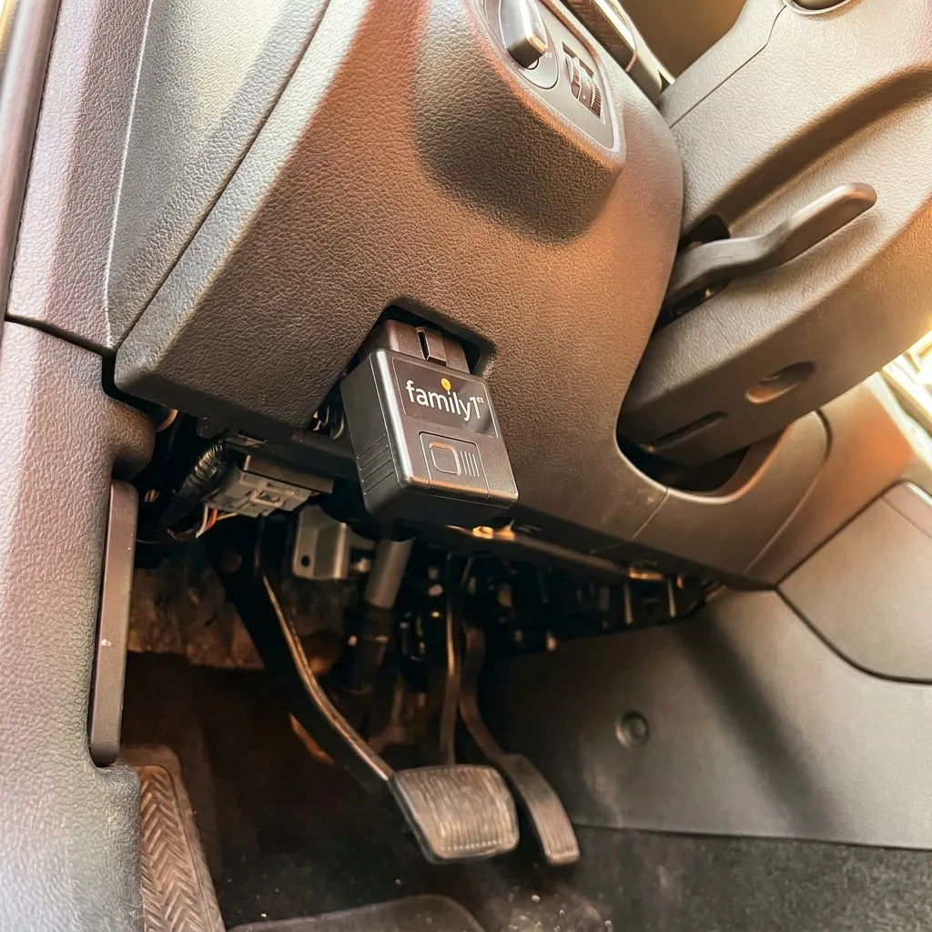 The OBD tracker plugged into the diagnostic port beneath a car's steering column